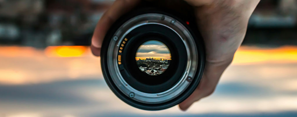 Immagine anteprima sezione Training and Development : mano che impugna un obbiettivo fotografico, che mostra al suo interno l'orizzonte di un città